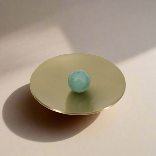 Small round bass dish with a green stone sphere  on a neutral background