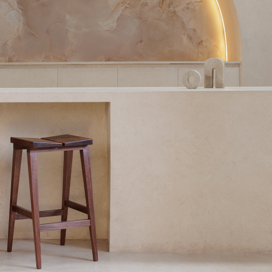 Wooden stool at a bench with a decorative travertine arch and candle holder in a minimalistic room with neutral tones