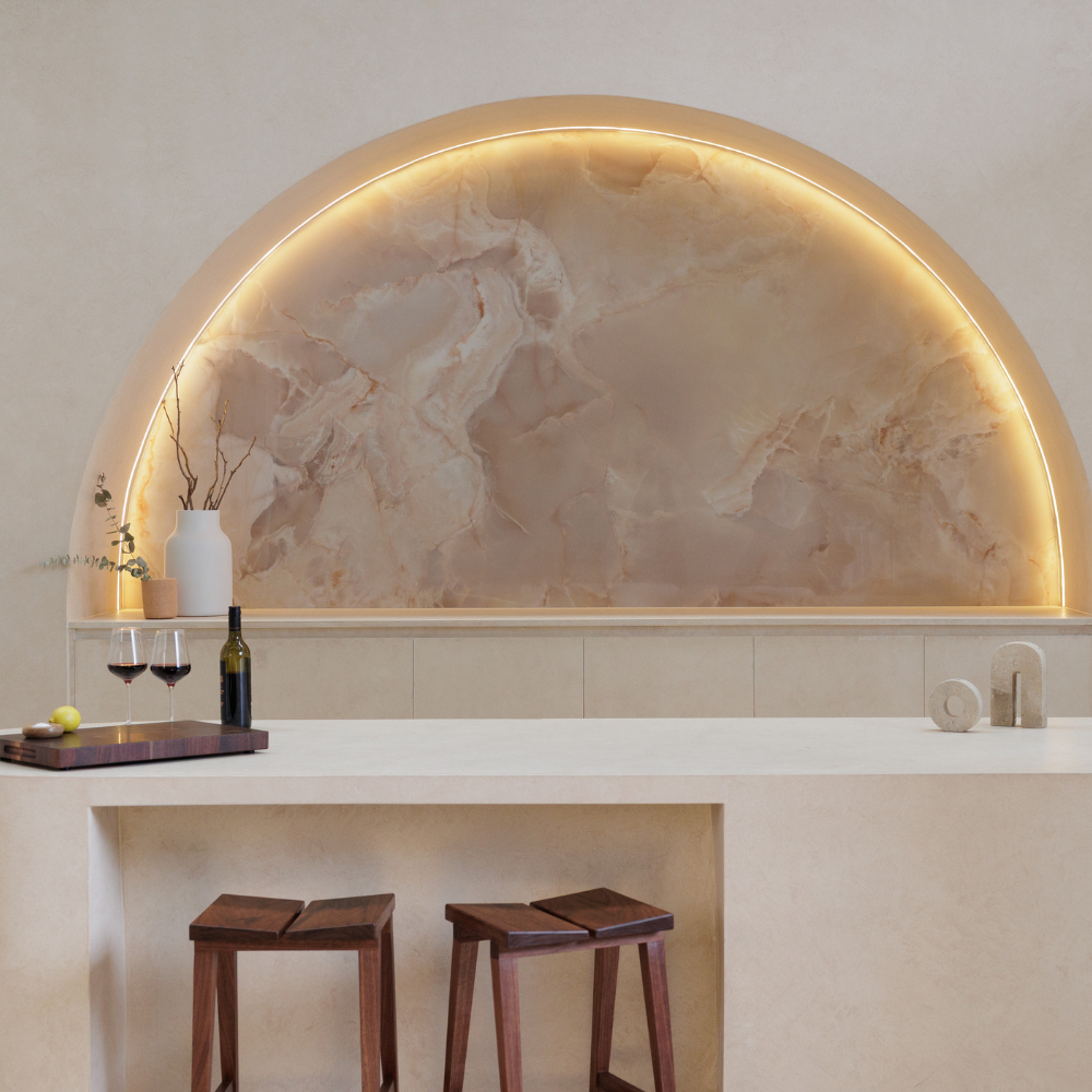 Modern kitchen with marble backsplash and wooden stools. Two travertine sculptures on benchtop with chopping board