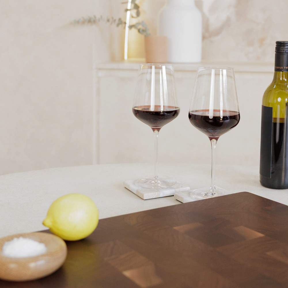 Two glasses of red wine on stone coasters with a lemon and a bottle of wine in the background.