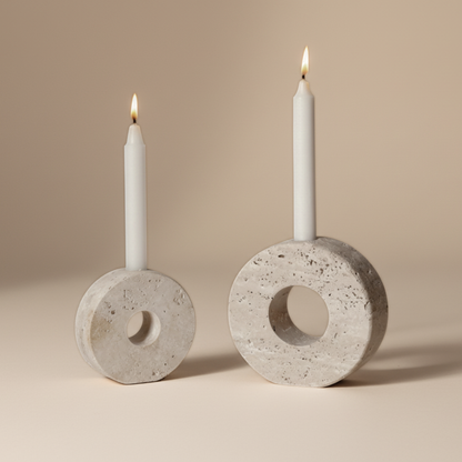 Two travertine candle holders with lit white candles on a beige background