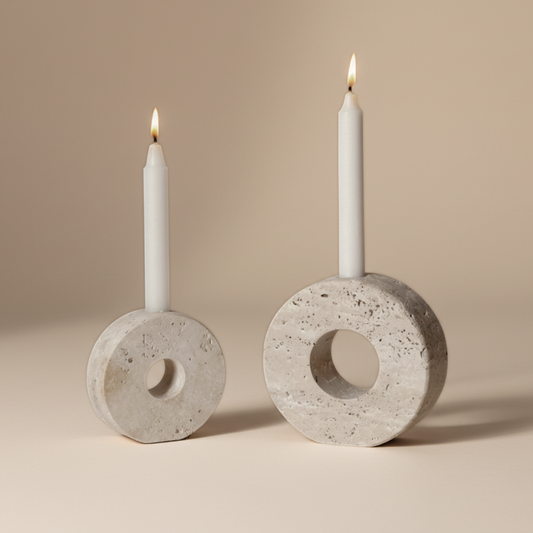 Two travertine candle holders with lit white candles on a beige background