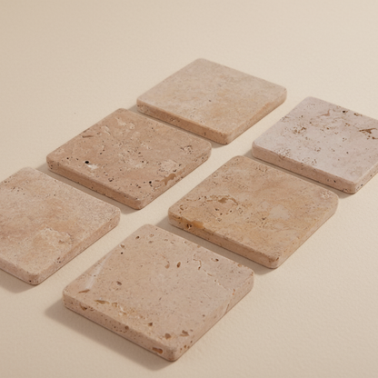 Set of six square travertine stone coasters on a beige background