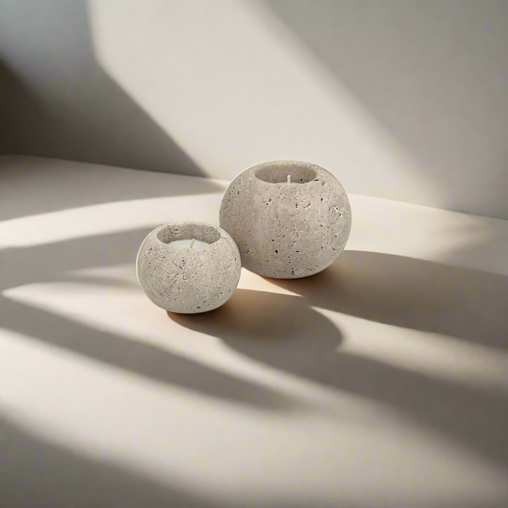 Two travertine candle holders casting shadows on a light surface.