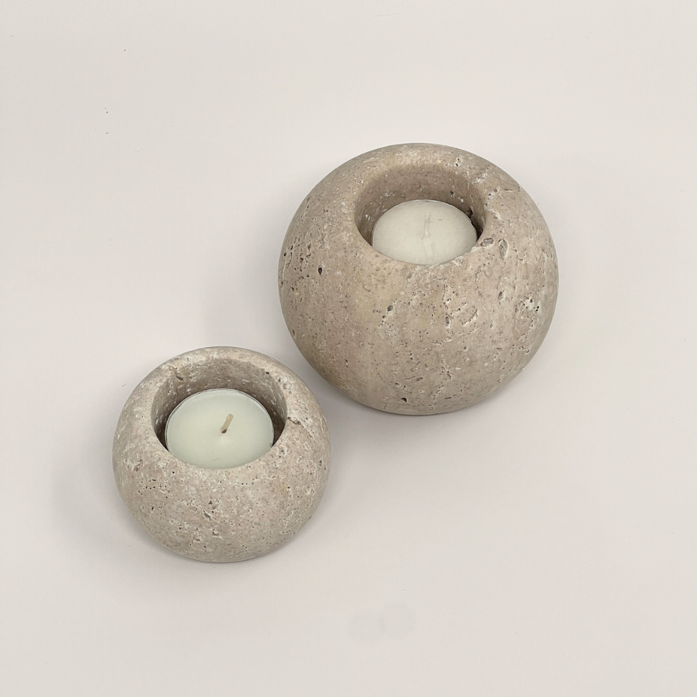 Two travertine candle holders with candles inside on a light grey background