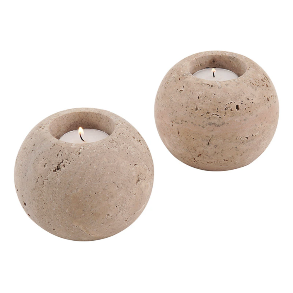 Two round travertine candle holders with candles inside on a white background
