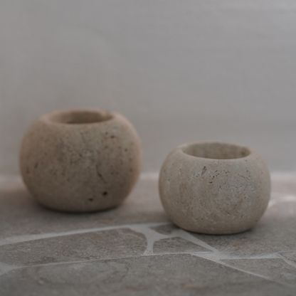 Two travertine candle holders on a stone surface with a neutral background
