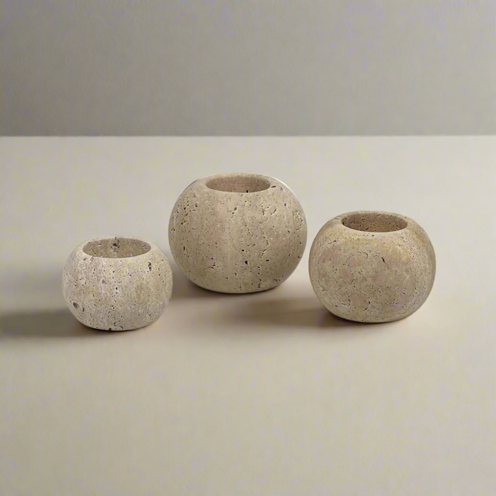 Three travertine candle holders of varying sizes on a light grey background