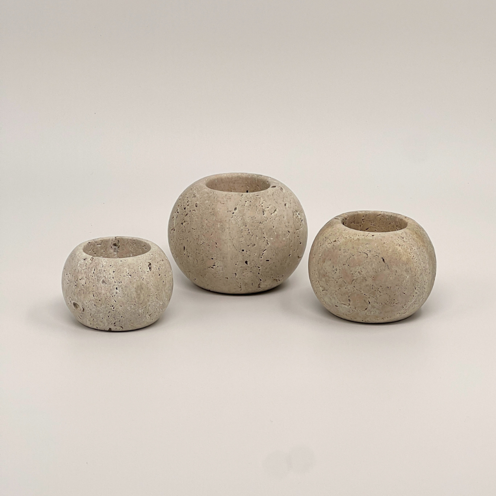 Three travertine candle holders of varying sizes on a light grey background