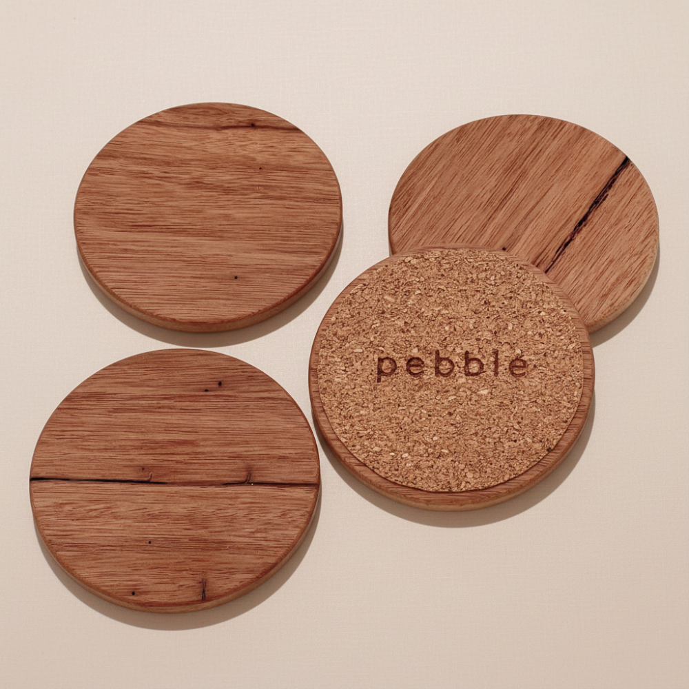 Four wooden coasters with cork bottom on a beige background, featuring the brand 'pebbie'.