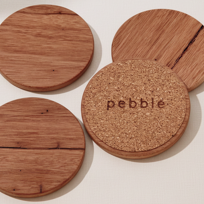 Wooden coasters with cork bottom and 'pebble' branding on a light background