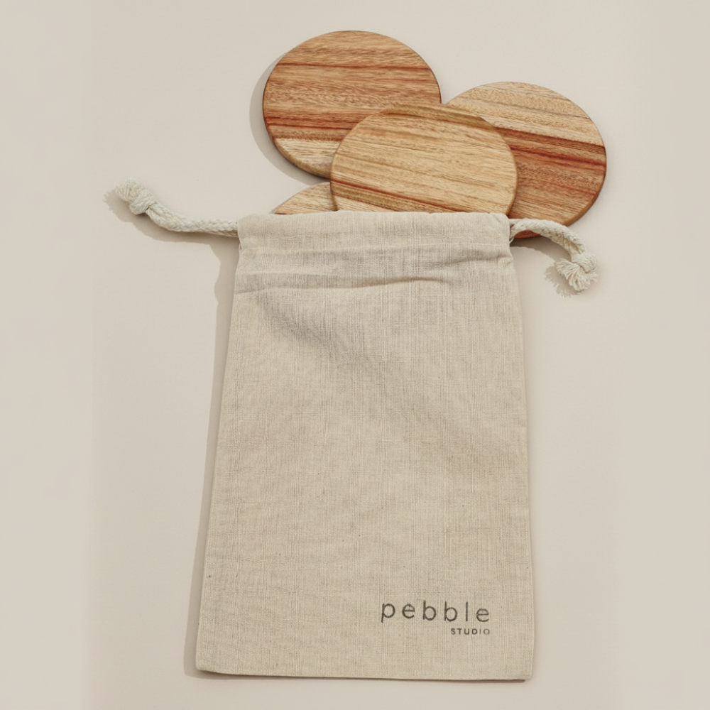 Four wooden coasters in a drawstring bag with 'Pebble Studio' branding on a beige background.
