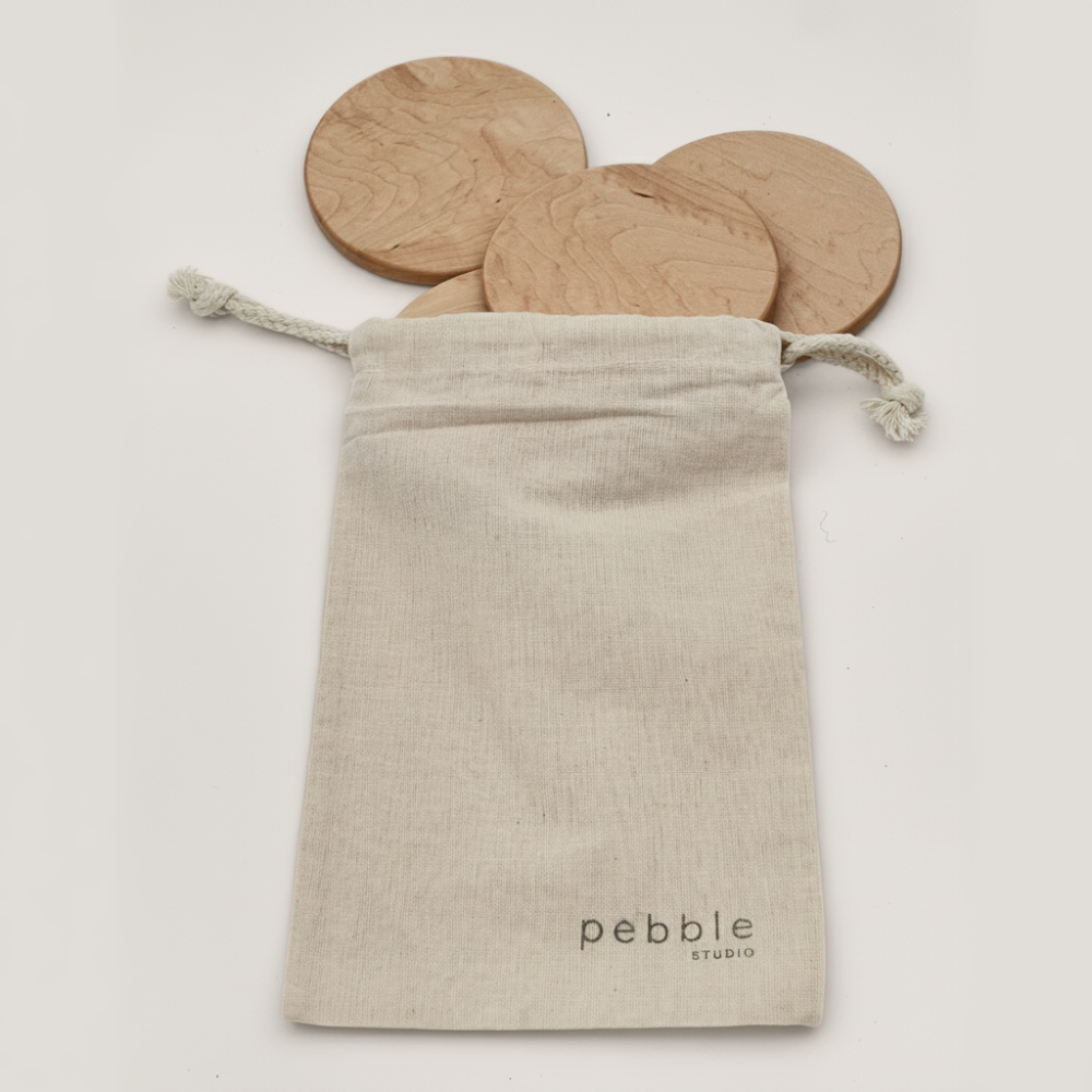 Wooden coasters in a drawstring bag with 'Pebble Studio' branding on a white background