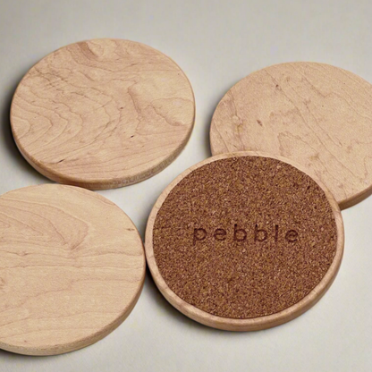 Set of wooden coasters with a cork base and 'pebble' branding on a light background