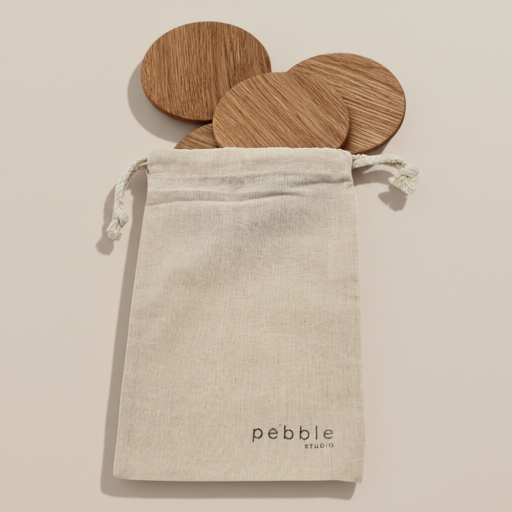 Wooden coasters in a drawstring bag with 'Pebble Studio' branding on a beige background