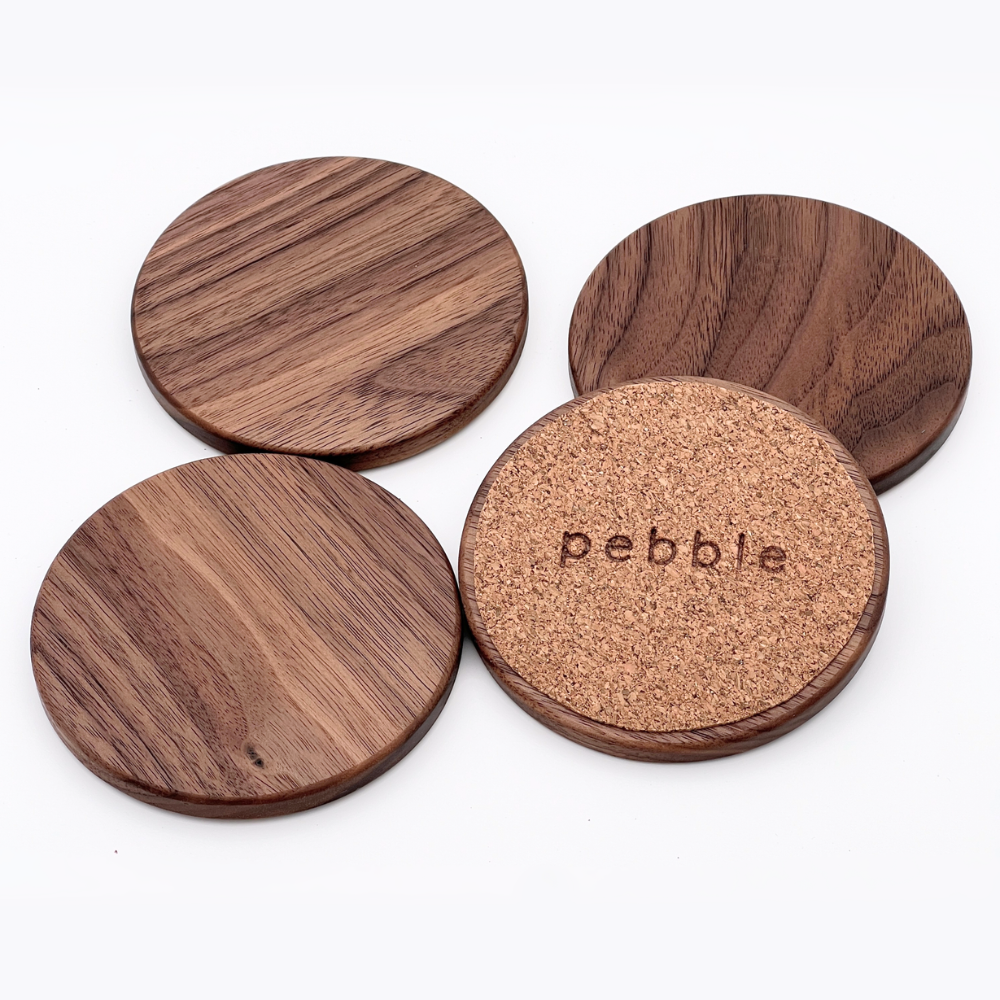 Four wooden coasters with cork bottom, branded 'Pebble', on a white background