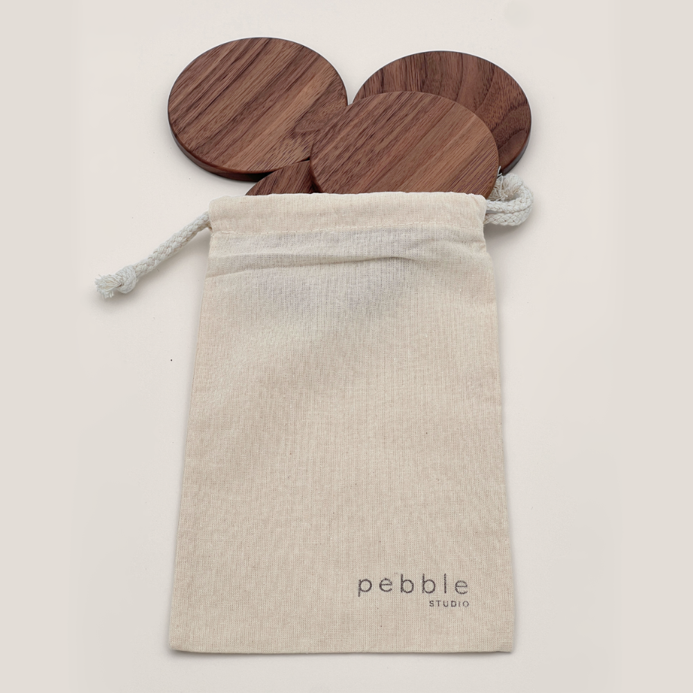 Wooden coasters in a calico bag with 'pebble studio' branding on a light background