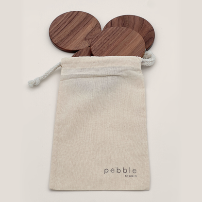 Wooden coasters in a calico bag with 'pebble studio' branding on a light background