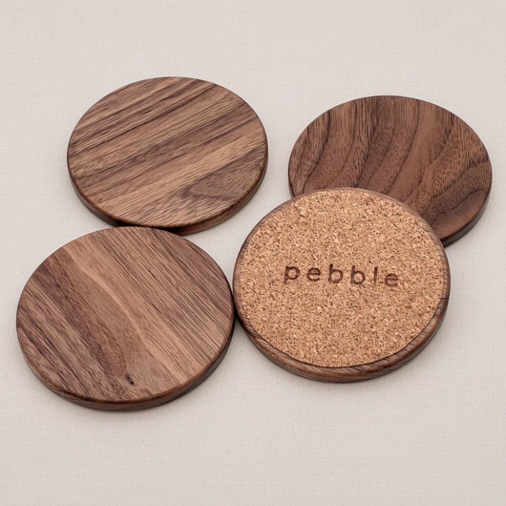Four wooden coasters with cork bottom, branded 'Pebble', on a light gray background.