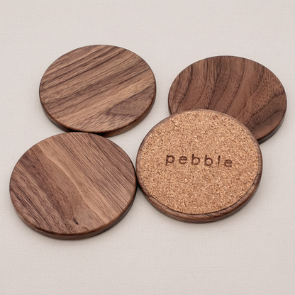 Four wooden coasters with cork bottom, branded 'Pebble', on a light gray background.
