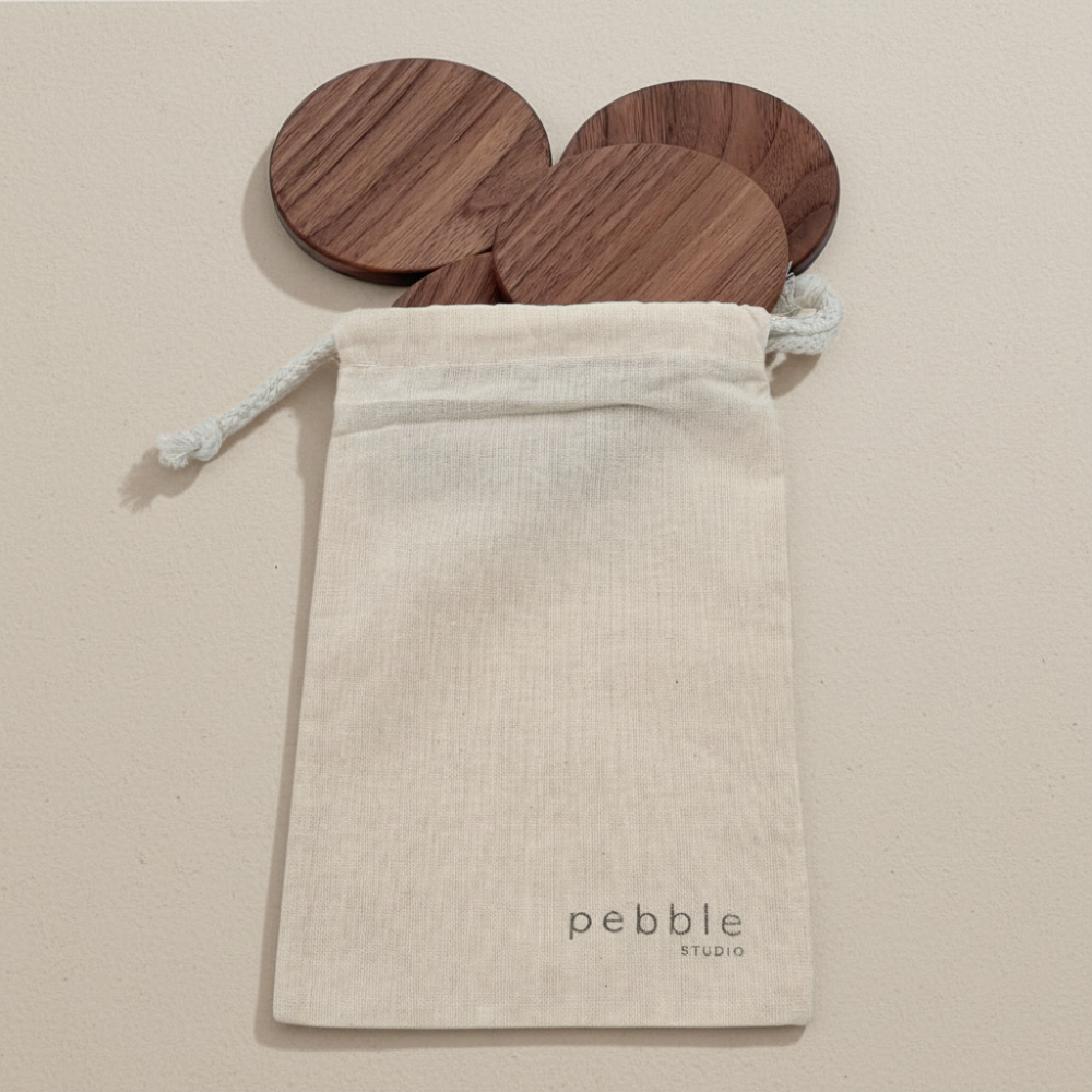 Wooden coasters in a 'Pebble Studio' drawstring bag against a beige background