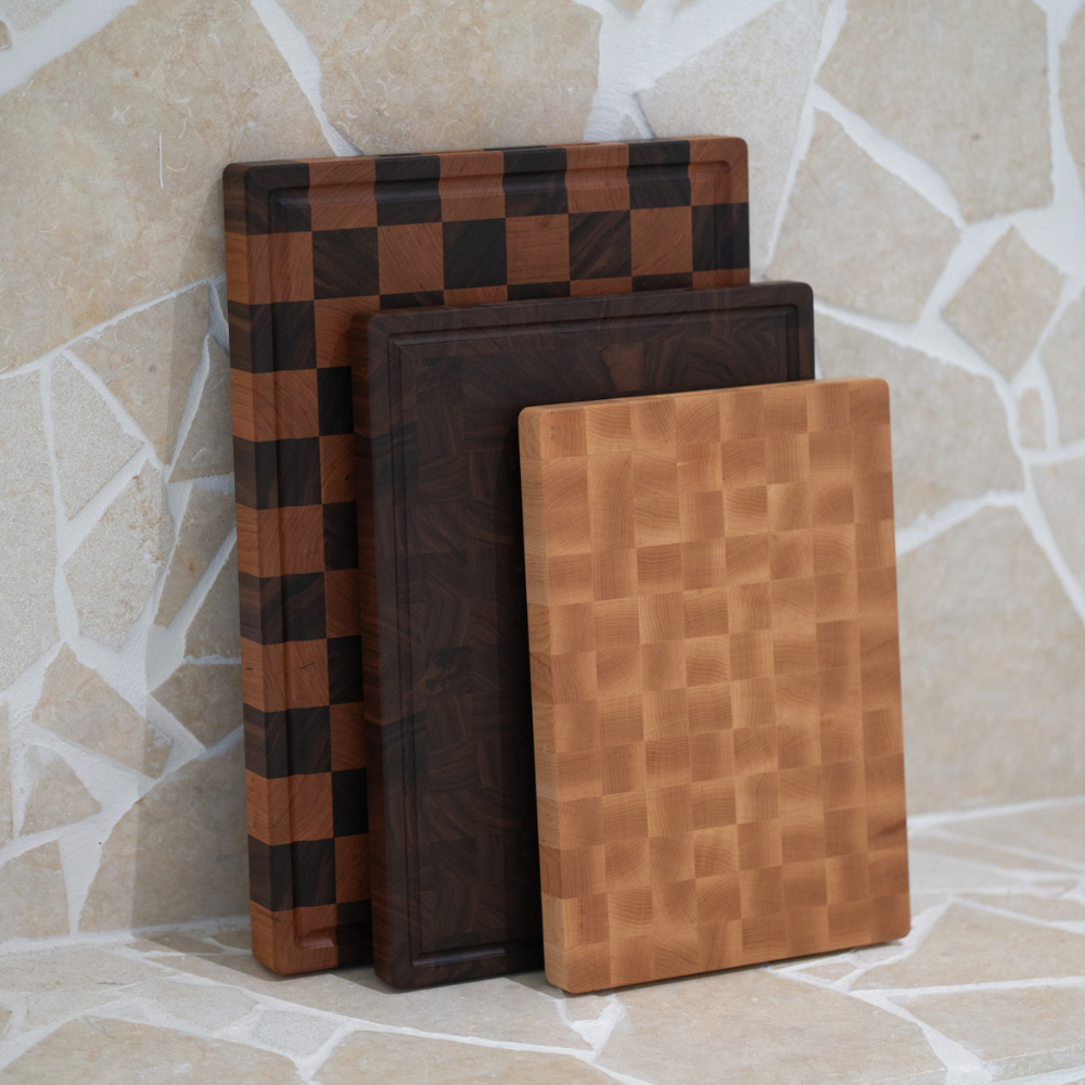 Three wooden end-grain chopping boards stacked against a stone wall.