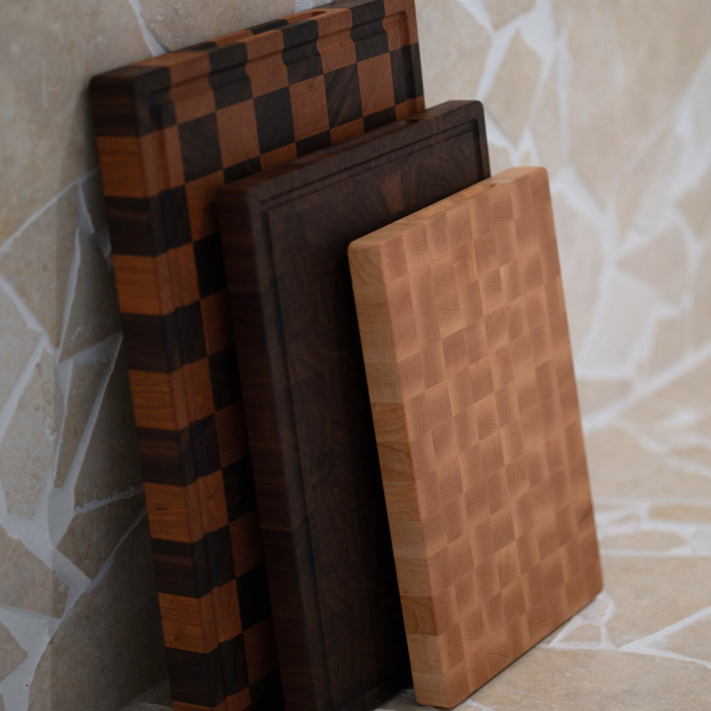 Three wooden end-grain chopping boards stacked against a tiled wall.