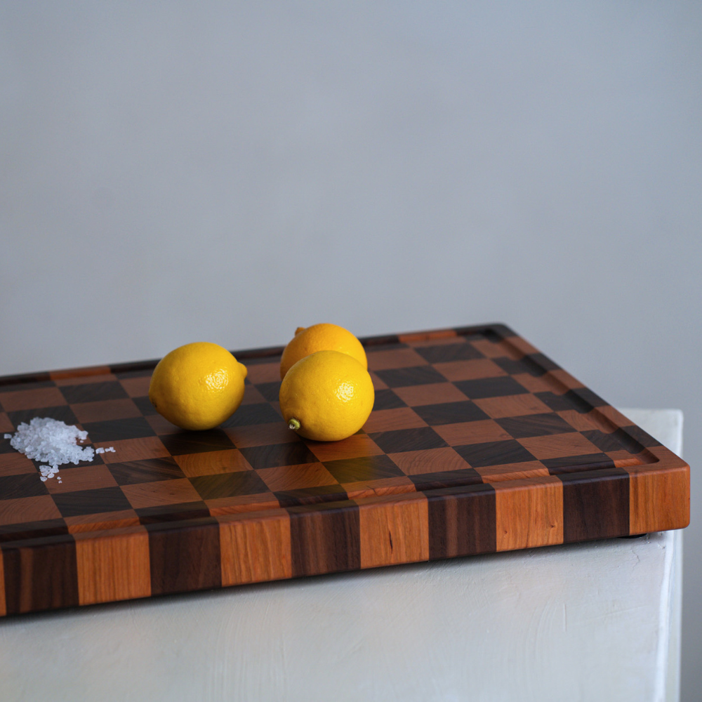 Wooden checkered chopping board with lemons on a neutral background
