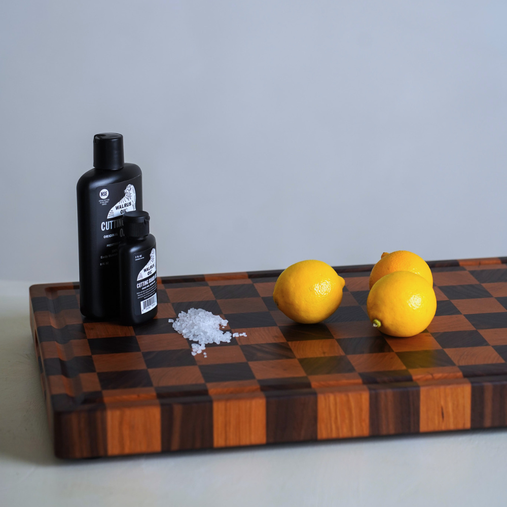 Two black bottles, a small pile of salt, and three lemons on a checkered wooden chopping board.