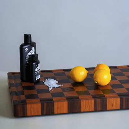 Two black bottles, a small pile of salt, and three lemons on a checkered wooden chopping board.