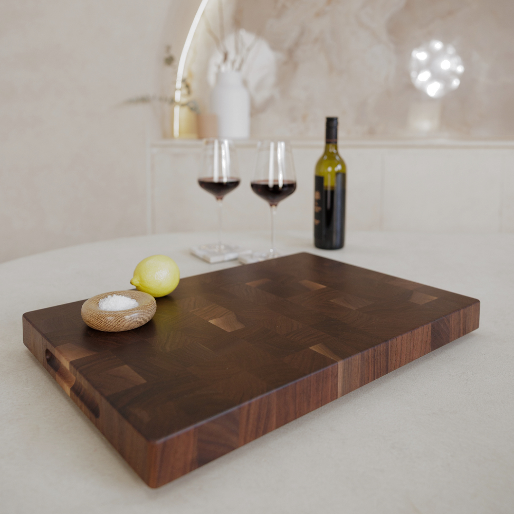 Wooden chopping board with a lemon, salt, two glasses of red wine, and a bottle on a white surface.
