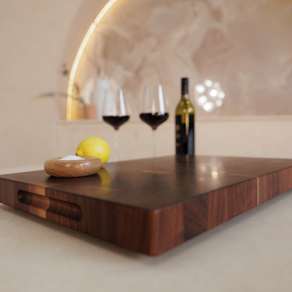 Wooden chopping board with wine glasses, bottle, and lemon on a countertop.