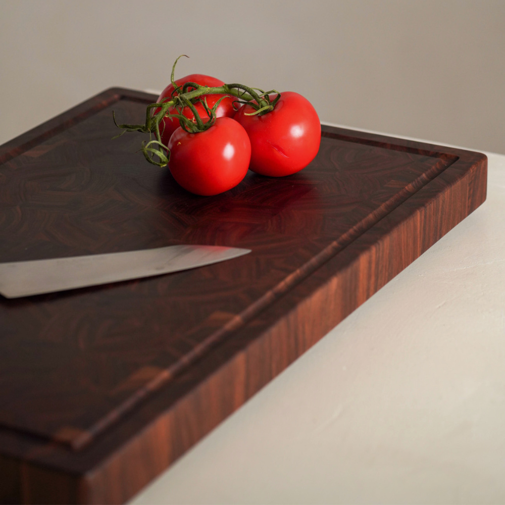 Three red tomatoes on a wooden chopping board with a knife.