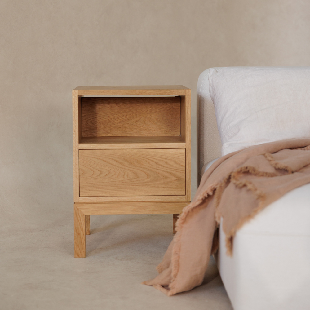 Wooden bedside table next to a bed with a beige blanket on a neutral background