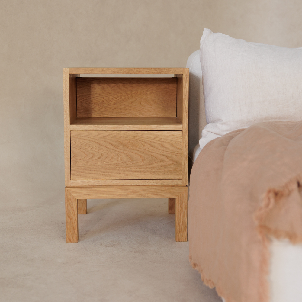 Wooden bedside table next to a bed with beige bedding