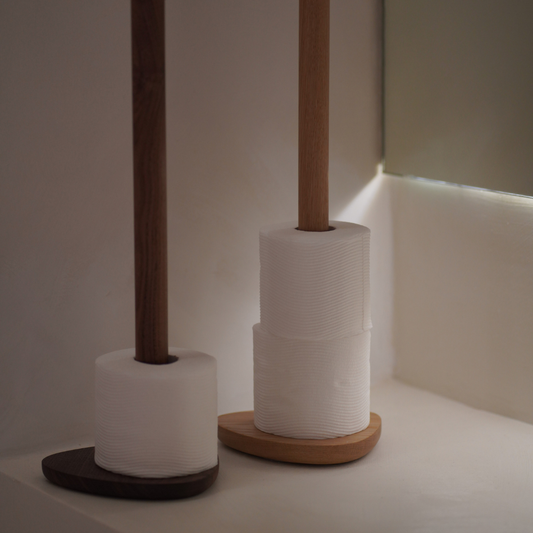 Toilet paper on two wood toilet roll stands against a neutral background