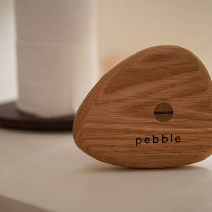 Base of wood toilet roll holder with 'pebble' branding on a neutral background