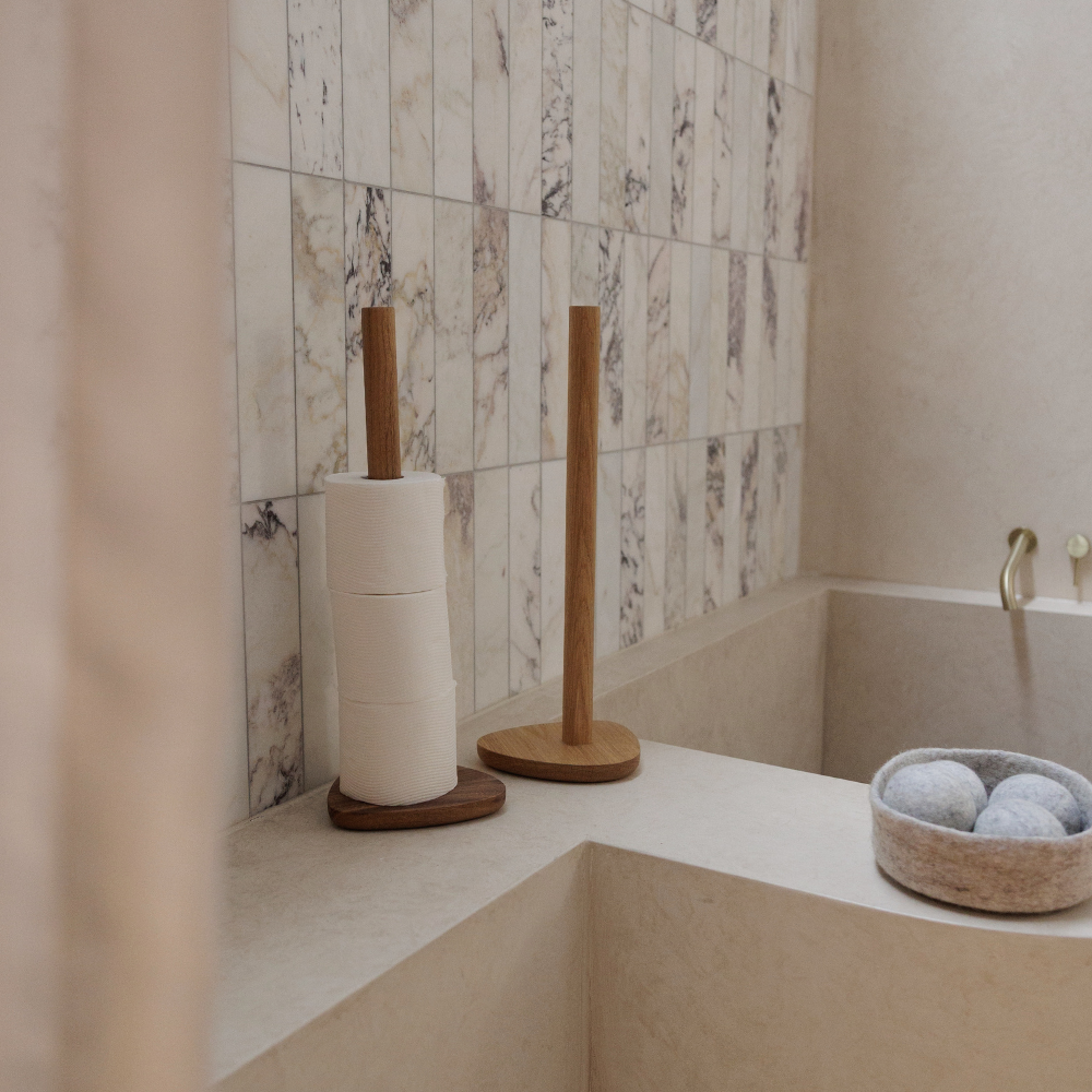 Bathroom corner with toilet paper holder, with decorative wool bowl  holding dryer balls.