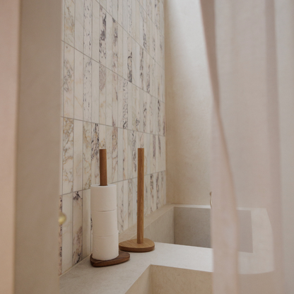 Two wood toilet roll holders in a bathroom with marble tiles.