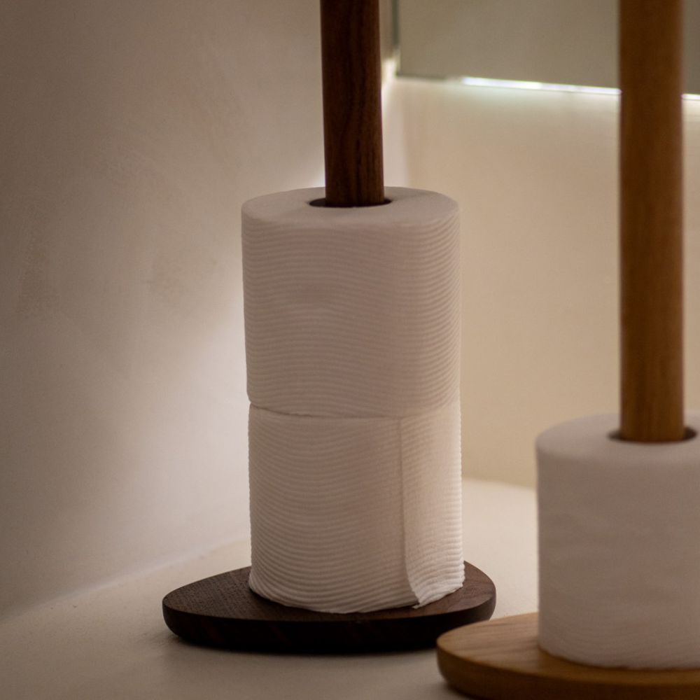 Two wood toilet roll holders with rolls of toilet paper against a neutral background