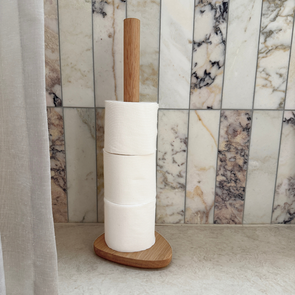 Wood toilet roll holder with white toilet paper against a marble wall.