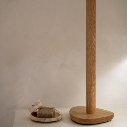 Wood toilet roll holder with a pebble shaped base on a neutral background