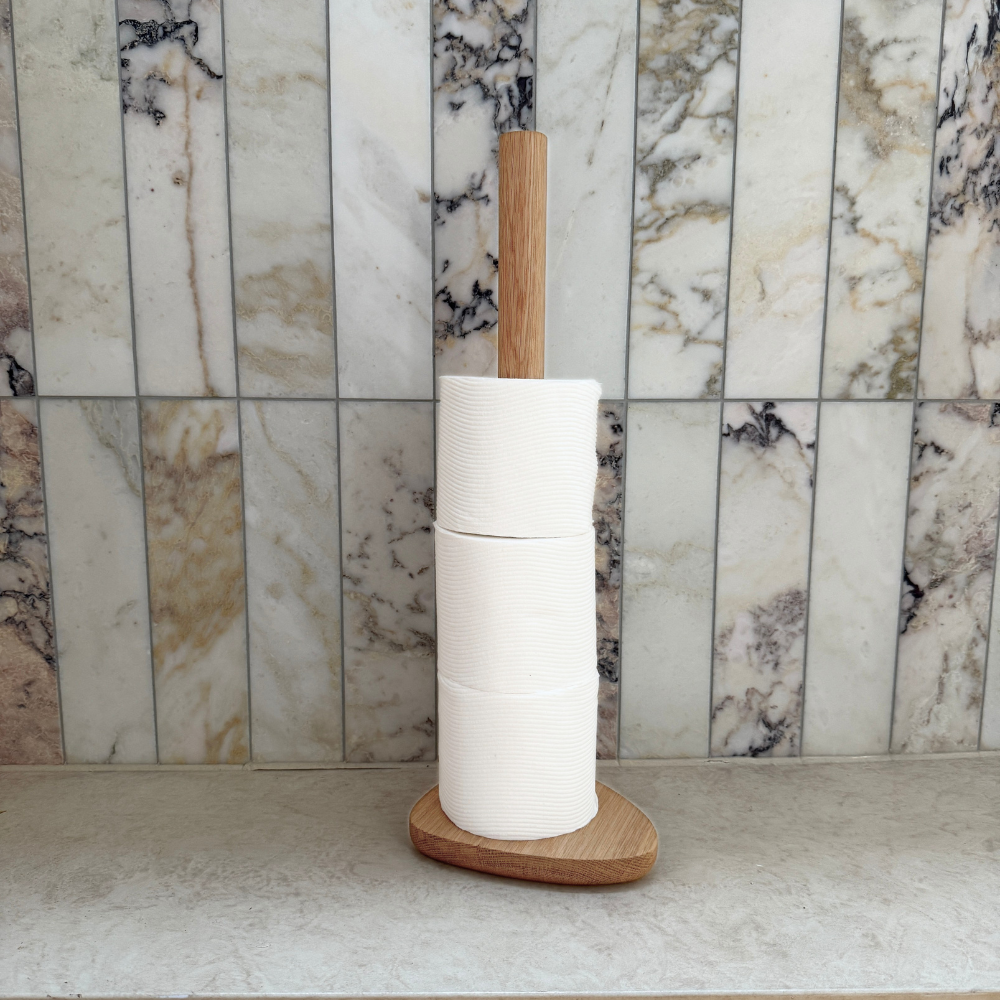 Wood toilet roll holder with toilet paper against a marble tiled wall.