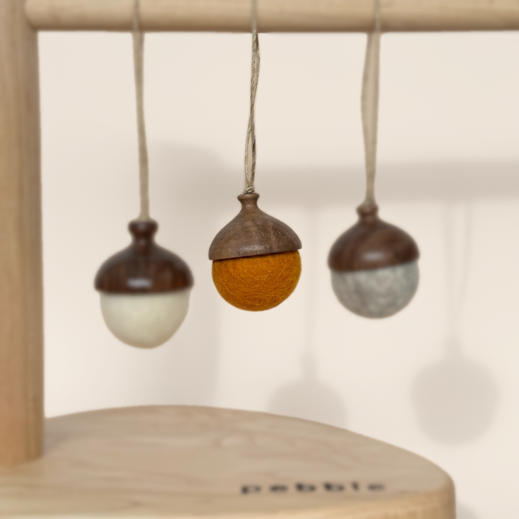 Three hand turned walnut and felt acorn ornaments with jute loop hanging from a wooden stand. Australian Made natural Christmas decoration for slow living