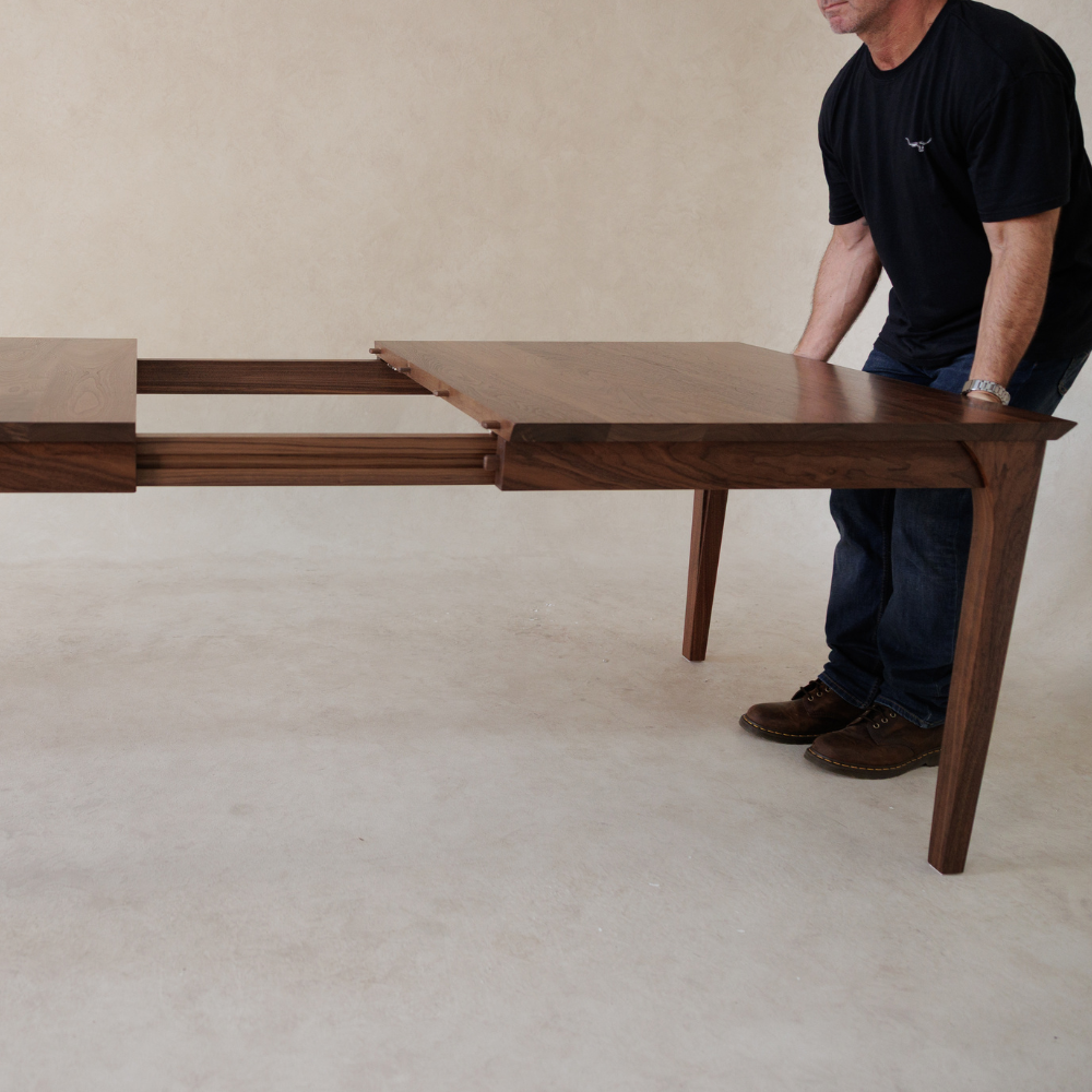 Man extending a wooden dining table on a plain background