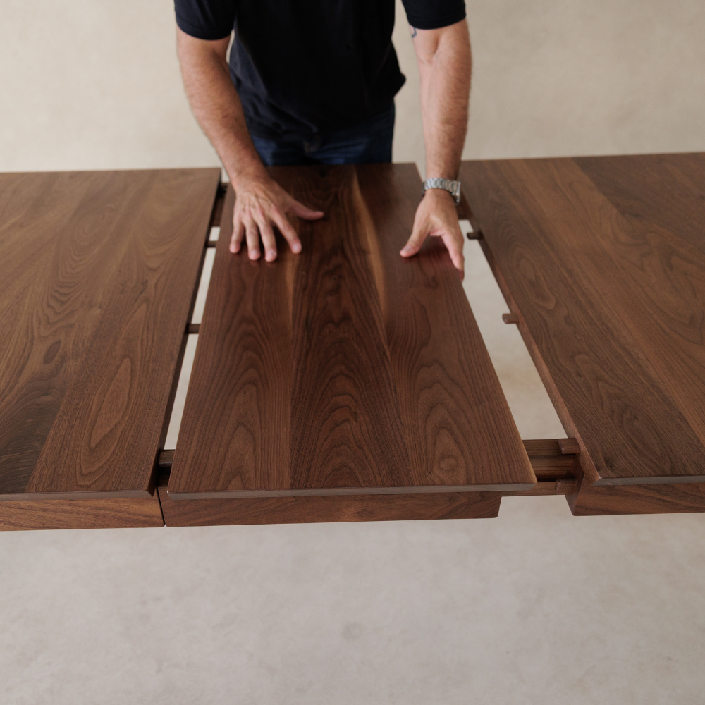 Person adding a wooden extension piece to a dining table on a neutral background