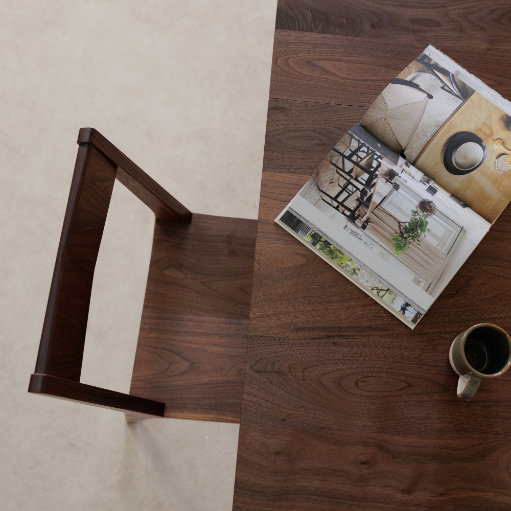 Wooden chair and table with a magazine and mug on a wooden floor.