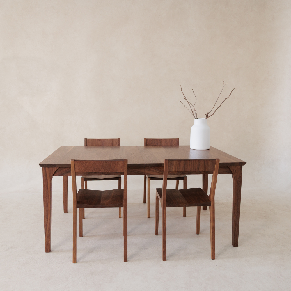 Wooden dining table with four chairs against a beige wall.