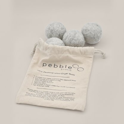 Four grey wool dryer balls with a drawstring bag labelled 'pebble studio' on a light background.
