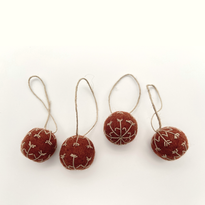 Four red felt ornaments with beige embroidery on a white background
